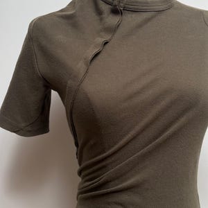 May include: A dark green short-sleeved shirt with a mandarin collar and a single button closure at the neckline.