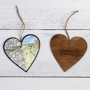 May include: Two wooden heart-shaped ornaments. One ornament is decorated with a map of a city, the other ornament has the text "Yvonne &hearts; Phil Christmas 2021".