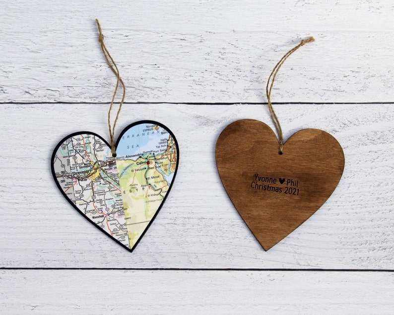 May include: Two wooden heart-shaped ornaments. One ornament is decorated with a map of a city, the other ornament has the text "Yvonne &hearts; Phil Christmas 2021".
