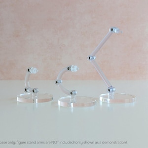 May include: Three clear plastic figure stands with adjustable arms. The stands are on clear acrylic bases.