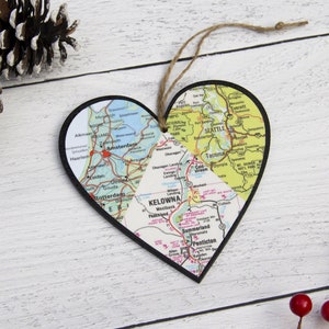 May include: A heart-shaped ornament made from a map of the United States. The ornament is divided into three sections, each showing a different region of the country. The top section shows the state of Washington, with the cities of Seattle and Tacoma labeled. The middle section shows the state of British Columbia, Canada, with the city of Kelowna labeled. The bottom section shows the state of Oregon, with the city of Portland labeled.