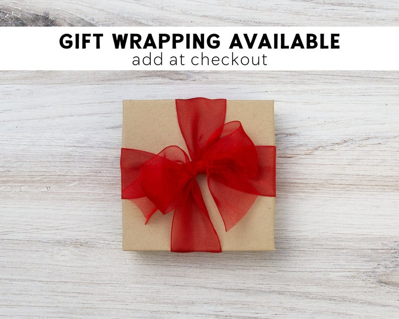 May include: A brown gift box with a red ribbon and bow. The box is on a white wooden surface. The text "GIFT WRAPPING AVAILABLE add at checkout" is above the box.
