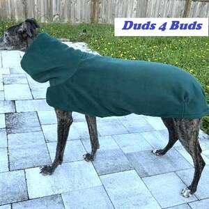 May include: A brindle dog wearing a dark green fleece dog coat. The coat has a hood and covers the dog's back and sides. The text "Duds 4 Buds" is in a white rectangle in the background.