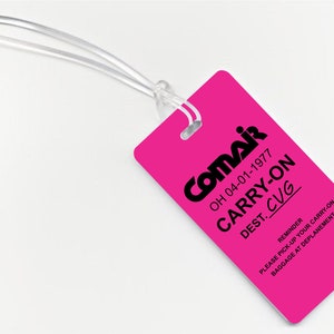 May include: Pink luggage tag with black text that reads "Comair OH 04-01-1977 CARRY-ON DEST. CUG" and a reminder to pick up carry-on baggage at deplanement.