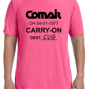 May include: A pink t-shirt with black text that reads "ComAir OH 04-01-1977 CARRY-ON DEST. CVG"