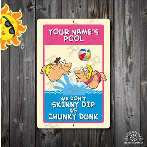 May include: A rectangular metal sign with a pink border and a cream-colored background. The sign features cartoon figures jumping into a pool, a beach ball, and the text "YOUR NAME'S POOL" and "WE DON'T SKINNY DIP WE CHUNKY DUNK". A cartoon sun is in the upper left corner.