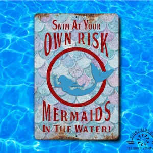 Pode incluir: Uma placa de metal retangular com um acabamento desgastado. A placa apresenta o texto "SWIM AT YOUR OWN RISK MERMAIDS IN THE WATER!" em letras vermelhas, com uma silhueta de sereia azul dentro de um círculo vermelho. O fundo tem um padrão de escamas de peixe.