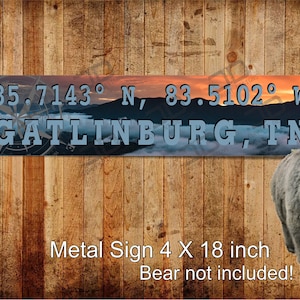 May include: Metal sign with a scenic mountain sunset background and the text "35.7143° N, 83.5102° W GATLINBURG, TN". The sign is 4 inches by 18 inches.