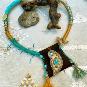 Peut inclure: Un collier turquoise et or avec un pendentif en daim brun orné d'un hibou coloré. Le collier est fait de divers matériaux, dont du fil, du cuir et des perles.