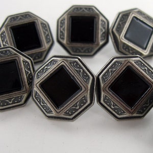 May include: Eight silver-toned buttons with black square centers and intricate decorative borders.