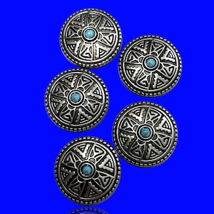 May include: Five silver-coloured, round buttons with an Aztec-inspired design. Each button features a central turquoise-coloured stone and intricate geometric patterns. The buttons are displayed against a vibrant blue background.
