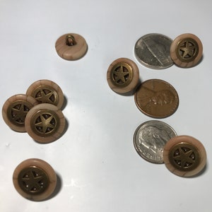 May include: A collection of eight beige buttons with a gold star design. The buttons are arranged on a white surface.