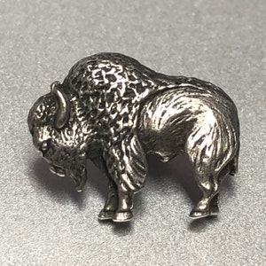 May include: A detailed silver-toned bison figurine. The sculpture depicts the animal in a standing position, with textured fur and defined features. The bison is a symbol of the American West.