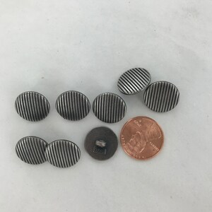 May include: Eight silver-toned buttons with a striped design. The buttons are approximately the size of a US penny.