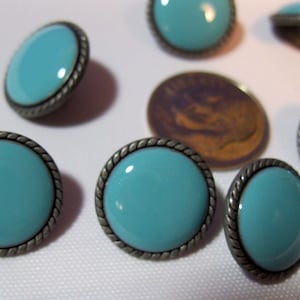 May include: A collection of round turquoise buttons with a silver-colored rope-like border. The buttons are arranged on a white surface. The buttons are approximately 0.75 inches in diameter.