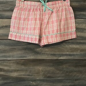 Pu&ograve; includere: Pantaloni corti da notte rosa e bianchi con motivo e bordatura blu chiaro. I pantaloncini hanno una vita con coulisse.