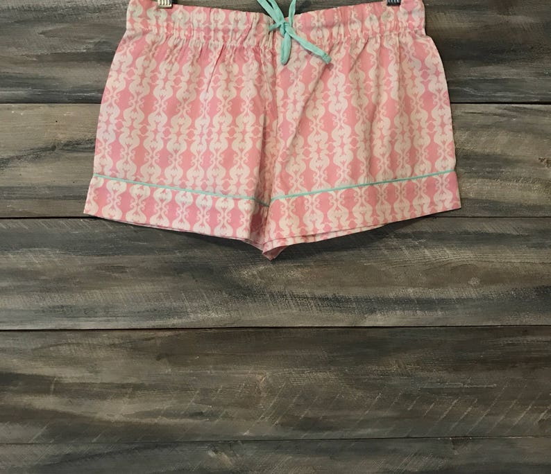 Pu&ograve; includere: Pantaloni corti da notte rosa e bianchi con motivo e bordatura blu chiaro. I pantaloncini hanno una vita con coulisse.