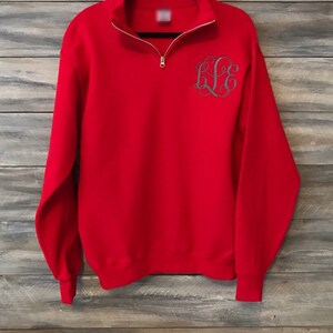May include: Red quarter-zip sweatshirt with a gray embroidered monogram on the front.