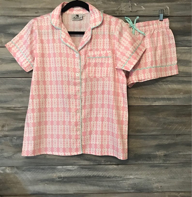 Pu&ograve; includere: Un pigiama rosa e bianco a fantasia con maniche corte e pantaloncini. La parte superiore ha una chiusura con bottoni sul davanti e un colletto. I pantaloncini hanno una cintura elastica e un laccio.