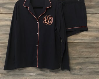 May include: Navy blue pajama set with long sleeves and shorts. The top has a button-up front and a pink trim. The shorts have a drawstring waist and a pink trim. The set is monogrammed with the letters "L.D." in a script font.