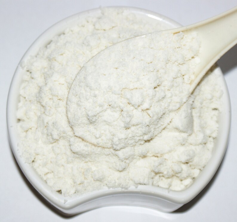 May include: A white ceramic bowl filled with a white powder, a white spoon is partially submerged in the powder.