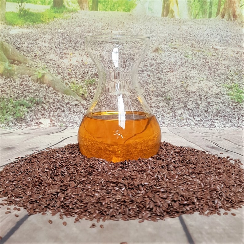 May include: A clear glass bottle filled with golden brown flaxseed oil sits on a pile of brown flax seeds.