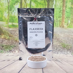 May include: A silver resealable bag of flaxseed baking flour. The bag is labelled "Flaxseed Baking Flour" and has a red seal. A small white bowl filled with the flour is in the foreground.