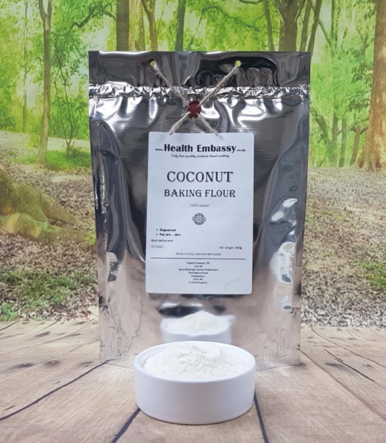 May include: A silver bag of 100% natural coconut baking flour. The bag is labeled "Coconut Baking Flour" and has a red seal. The bag is sitting on a wooden surface with a white bowl of coconut flour in front of it.