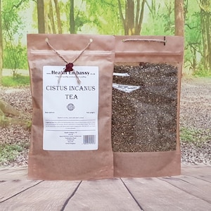 May include: A brown paper bag with a white label that reads "Cistus Incanus Tea" and a clear plastic bag filled with dried herbs. The bag is sitting on a wooden surface.