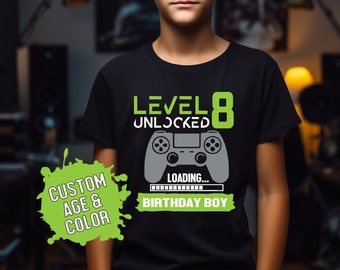 Könnte beinhalten: Schwarzes T-Shirt mit einem grünen und grauen Grafik-Videospiel-Controller. Der Text "Level 8 Unlocked" und "Loading... Birthday Boy" befindet sich auf dem Shirt.