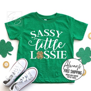 May include: Green t-shirt with white text that says "Sassy little Lossie" with a gold glitter shamrock.