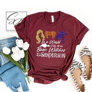 May include: A maroon t-shirt with a white graphic that says "In a world full of basic witches be a Sanderson". The graphic also includes three silhouettes of the Sanderson sisters from the movie Hocus Pocus.