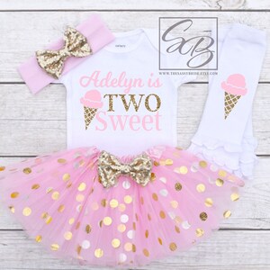 Puede incluir: Conjunto de cumplea&ntilde;os de helado rosa y dorado para un ni&ntilde;o de dos a&ntilde;os. El conjunto incluye un body blanco con el texto "Adelyn is Two Sweet" y un gr&aacute;fico de cono de helado, una falda de tul rosa con lunares dorados, una diadema rosa con un lazo dorado y polainas blancas con un gr&aacute;fico de cono de helado.
