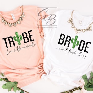 May include: Two white t-shirts with a cactus graphic and text. The first shirt says "Trybe" with a green glitter cactus and the text "Lisa's Bachelorette". The second shirt says "Bride...can't touch this!" with a green glitter cactus.