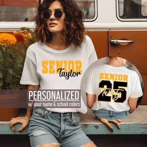 Pu&ograve; includere: Maglietta bianca con il testo "SENIOR Taylor" in lettere gialle e nere. Il retro della maglietta ha il testo "SENIOR 25" in lettere nere e gialle. Il testo "PERSONALIZZATO con il tuo nome e i colori della tua scuola" &egrave; sotto la maglietta.