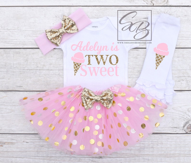 Puede incluir: Conjunto de cumplea&ntilde;os de helado rosa y dorado para un ni&ntilde;o de dos a&ntilde;os. El conjunto incluye un body blanco con el texto "Adelyn is Two Sweet" y un gr&aacute;fico de cono de helado, una falda de tul rosa con lunares dorados, una diadema rosa con un lazo dorado y polainas blancas con un gr&aacute;fico de cono de helado.
