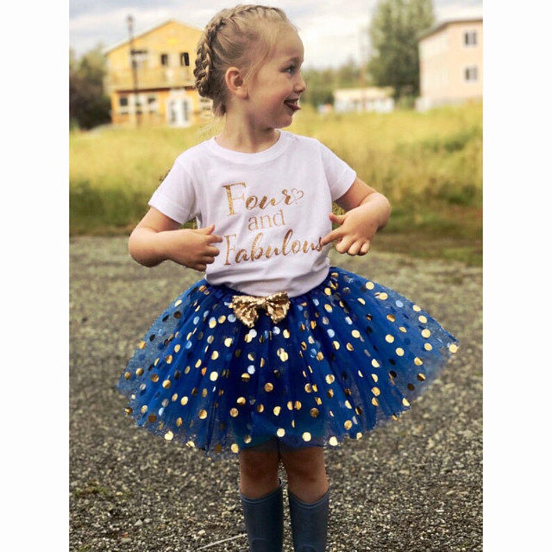 May include: A young girl wearing a white t-shirt with gold glitter text that says "Four and Fabulous" and a blue tulle skirt with gold polka dots.