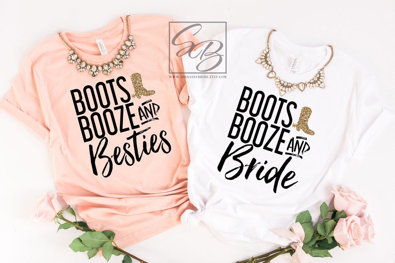 May include: Two t-shirts, one peach and one white, with the text "Boots, Booze, and Besties" and "Boots, Booze, and Bride" in black script. Each shirt has a gold glitter boot graphic. A necklace is draped on each shirt.