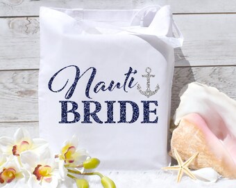 Può includere: Borsa tote in tela bianca con un design glitter blu navy che dice "Nauti Bride" con un'ancora glitter argentata.