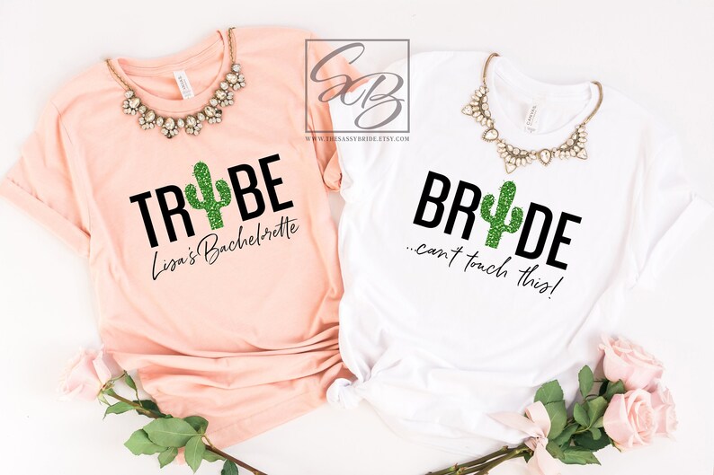 May include: Two white t-shirts with a cactus graphic and text. The first shirt says "Trybe" with a green glitter cactus and the text "Lisa's Bachelorette". The second shirt says "Bride...can't touch this!" with a green glitter cactus.