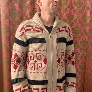 May include: A beige knitted cardigan with a zipper closure. The cardigan features a geometric pattern in red, black, and white.
