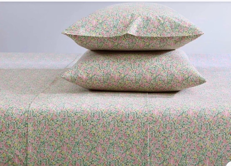 May include: A bed set featuring a floral pattern in pink, green, and yellow. Two pillows are stacked on top of a matching sheet. The bedding has a delicate, all-over floral design, creating a soft and inviting aesthetic. The sheets and pillowcases are made of a lightweight fabric.