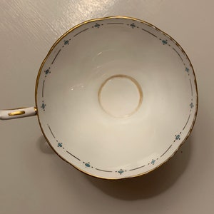 Puede incluir: Taza de t&eacute; blanca con borde y asa dorados, con un delicado patr&oacute;n de puntos azules a lo largo del borde. El interior muestra una mancha marr&oacute;n claro. Un dise&ntilde;o cl&aacute;sico para t&eacute; o caf&eacute;.