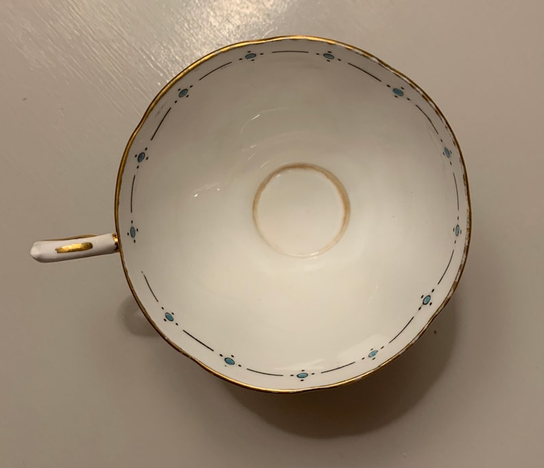 Puede incluir: Taza de t&eacute; blanca con borde y asa dorados, con un delicado patr&oacute;n de puntos azules a lo largo del borde. El interior muestra una mancha marr&oacute;n claro. Un dise&ntilde;o cl&aacute;sico para t&eacute; o caf&eacute;.
