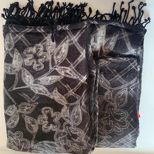 May include: A black and white patterned scarf with a fringe border. The pattern features a repeating design of stylized leaves and flowers.
