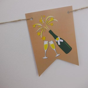 Op de afbeelding: Een beige banner met een illustratie van een champagnefles en twee glazen. De fles is groen met een wit etiket en de champagne is geel. De banner is geregen aan een natuurlijk touw.