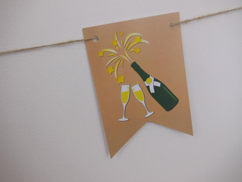 Op de afbeelding: Een beige banner met een illustratie van een champagnefles en twee glazen. De fles is groen met een wit etiket en de champagne is geel. De banner is geregen aan een natuurlijk touw.