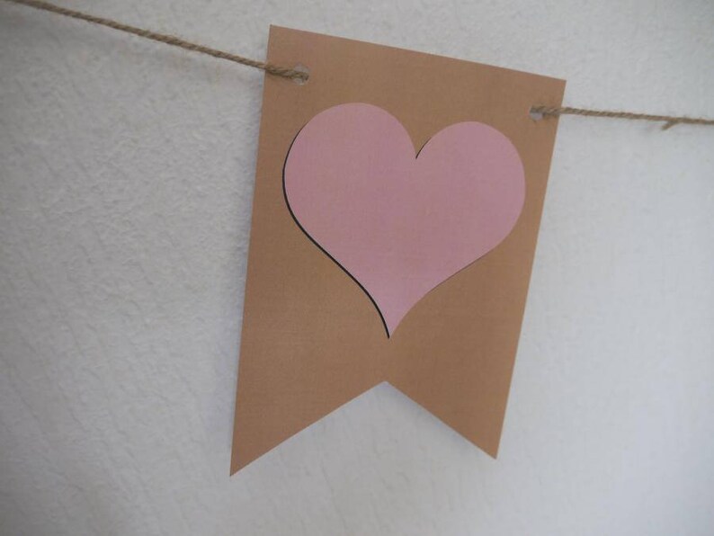 Op de afbeelding: Een bruine papieren banner met een uitgesneden roze hart. De banner is vastgemaakt met touw.