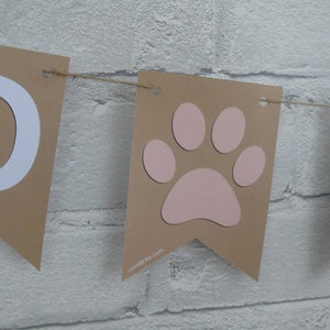 May include: A brown banner with white letters spelling "Pawty" and a pink paw print. The banner is strung with twine.