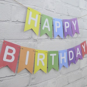 May include: A colorful banner with the words "HAPPY BIRTHDAY" in white letters. The pennants are in rainbow colors and strung on a natural twine, perfect for a birthday celebration.